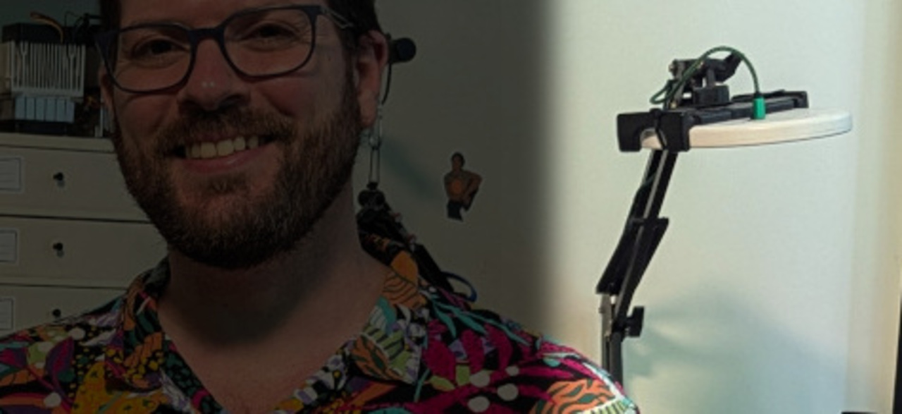 Spode at his desk with the SAD lamp visible on a phone arm behind him